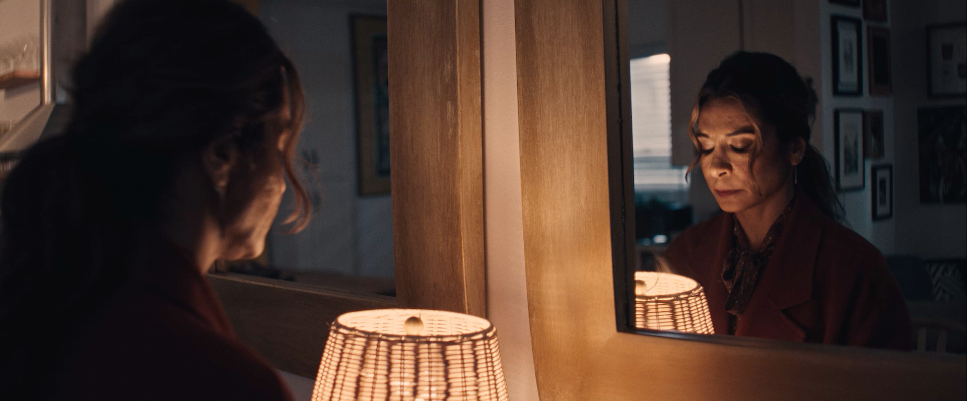 A woman turns a lamp on, her face reflected in a mirror